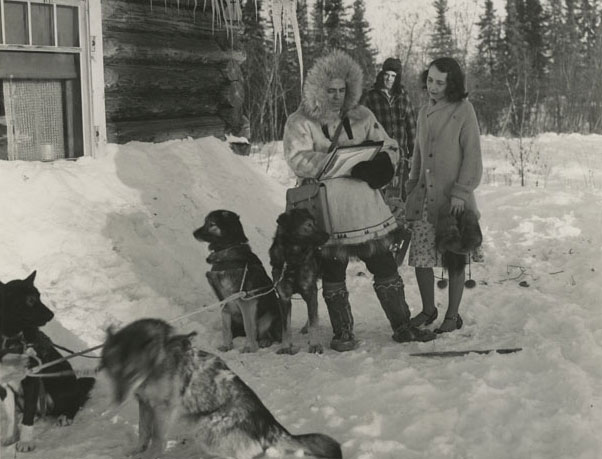 Image of Fairbanks, Alaska - The Census in Alaska. William F. Arends (Left), Assistant to the Alaska Supervisor, in charge of the Sixteenth Decennial Census in the Fourth Judicial Division, obtains confidential census information form Mrs. Ellen Bradley (right) so Mike Agababa, (center background) dog musher for Mr. Arends, waits out of earshot. The answers to census questions must be kept secret no matter where the census is being taken. Census-taking in Alaska began last October. Photo by Dwight Hammack, U.S. Bureau of the Census.
