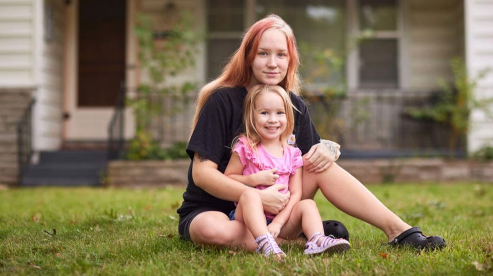 New MFH iconic photo of young white woman and smiling child seated in the grass of a front lawn