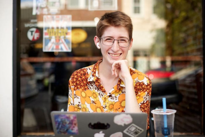 New MFH iconic photo of smiling person seated at an outdoor cafe, working on a laptop