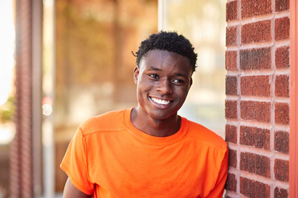 New MFH iconic photo of smiling young Black Man standing outside, leaning against brick wall 