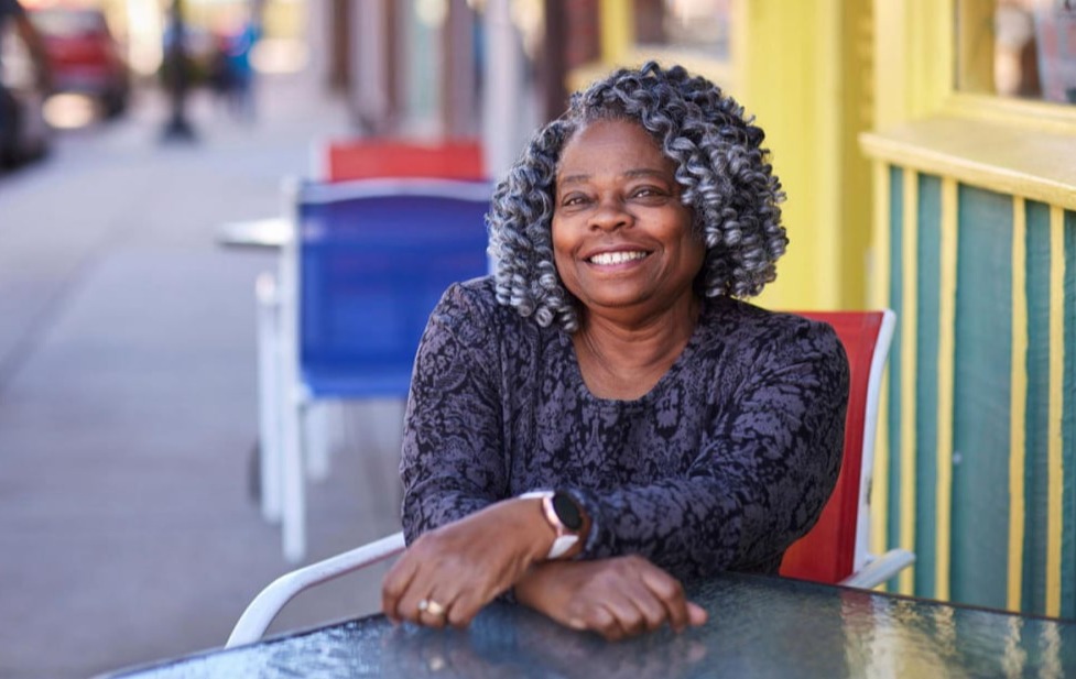 New MFH iconic photo of smiling Black woman seated at outdoor cafe table