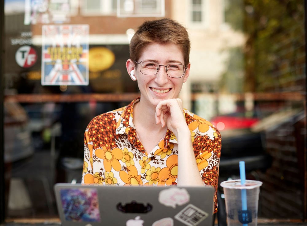 Person at outdoor cafe, working on laptop computer and smiling at the camera