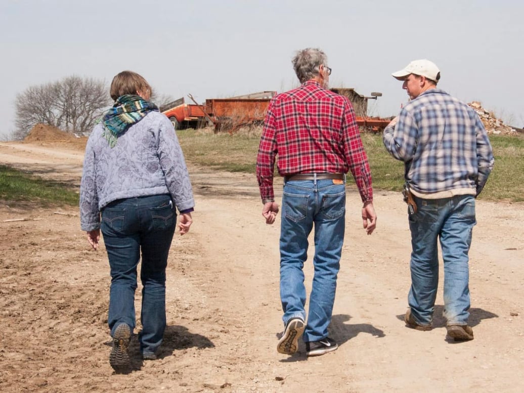 Three people walking on a dirt farm road, learning about how to become farmers