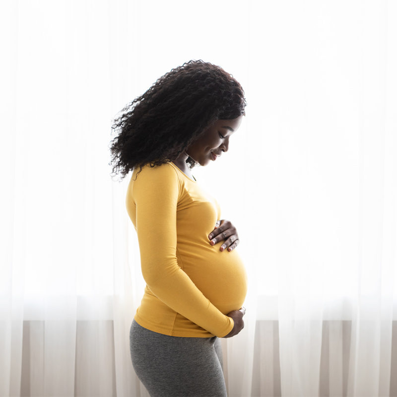 Black woman in profile cradling her baby bump