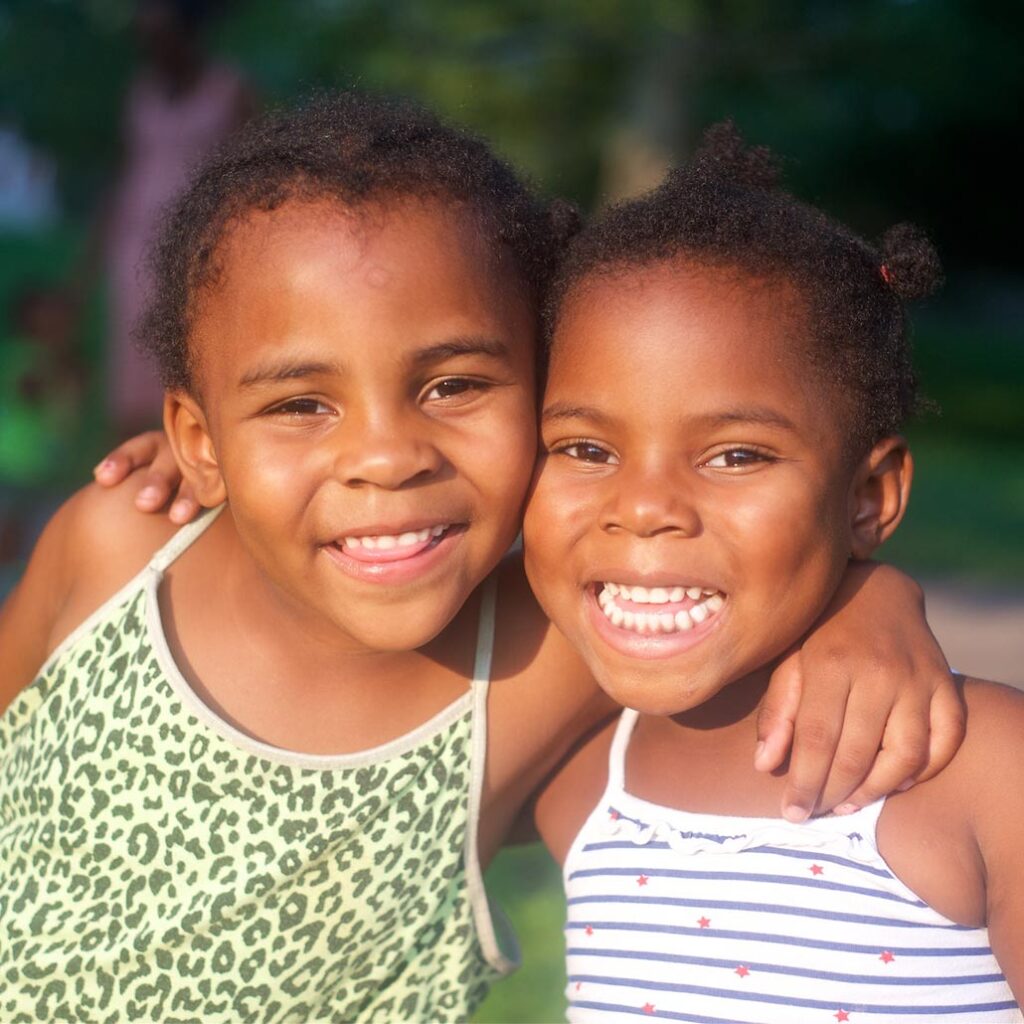 Photo of two little girls smiling in the sunlight with their arms around each other