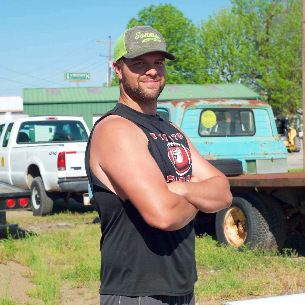 Photo of young man standing in grassy lot with trucks in background