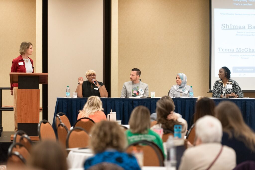 A diverse panel presents from table in front of a crowd at the Advocates’ Retreat