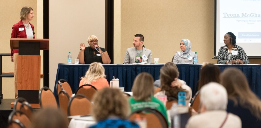 A diverse panel presents from table in front of a crowd at the Advocates’ Retreat