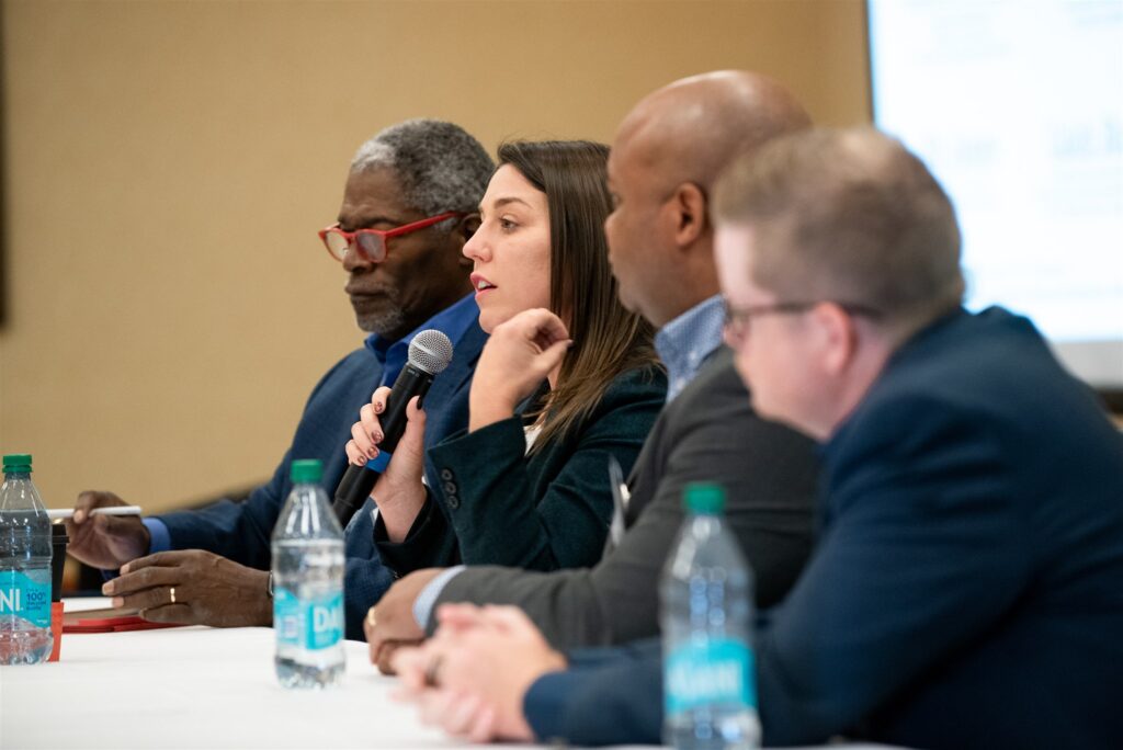 A diverse panel presents from table in front of a crowd at the Advocates’ Retreat