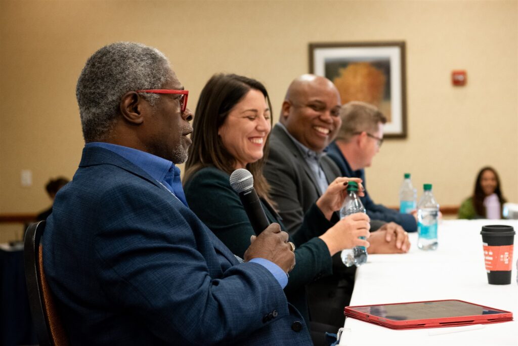 A diverse panel presents from table in front of a crowd at the Advocates’ Retreat