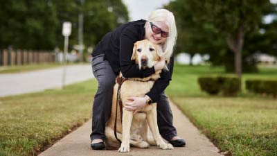Woman with dark glasses hugging guide dog on the sidewalk