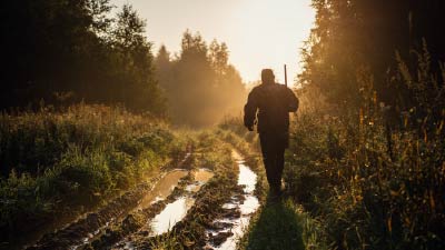 Hunter walks down rural path at dawn