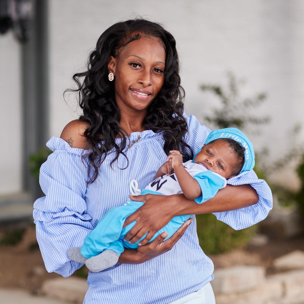 Smililing Black mother cradles small infant outdoors